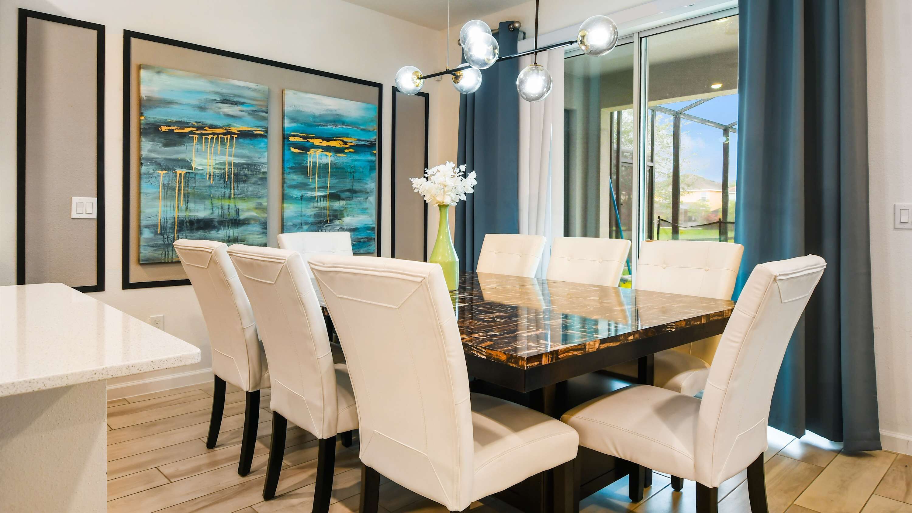 Une salle à manger avec une table en marbre et des chaises blanches, de grandes peintures abstraites accrochées aux murs et une vue par les fenêtres.