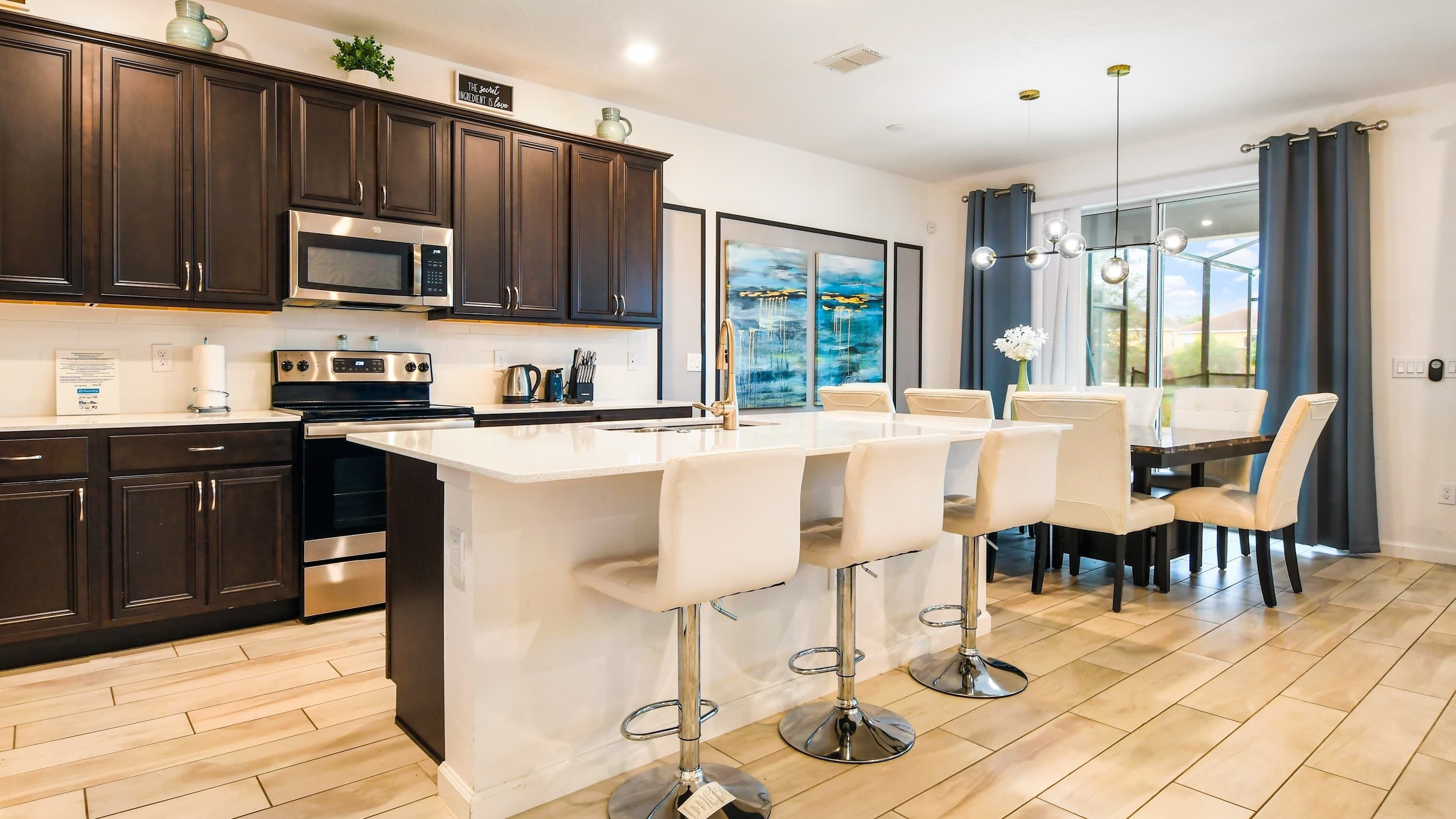 Una cocina moderna con gabinetes oscuros, una isla central con taburetes altos y una zona de comedor con mesa y sillas.