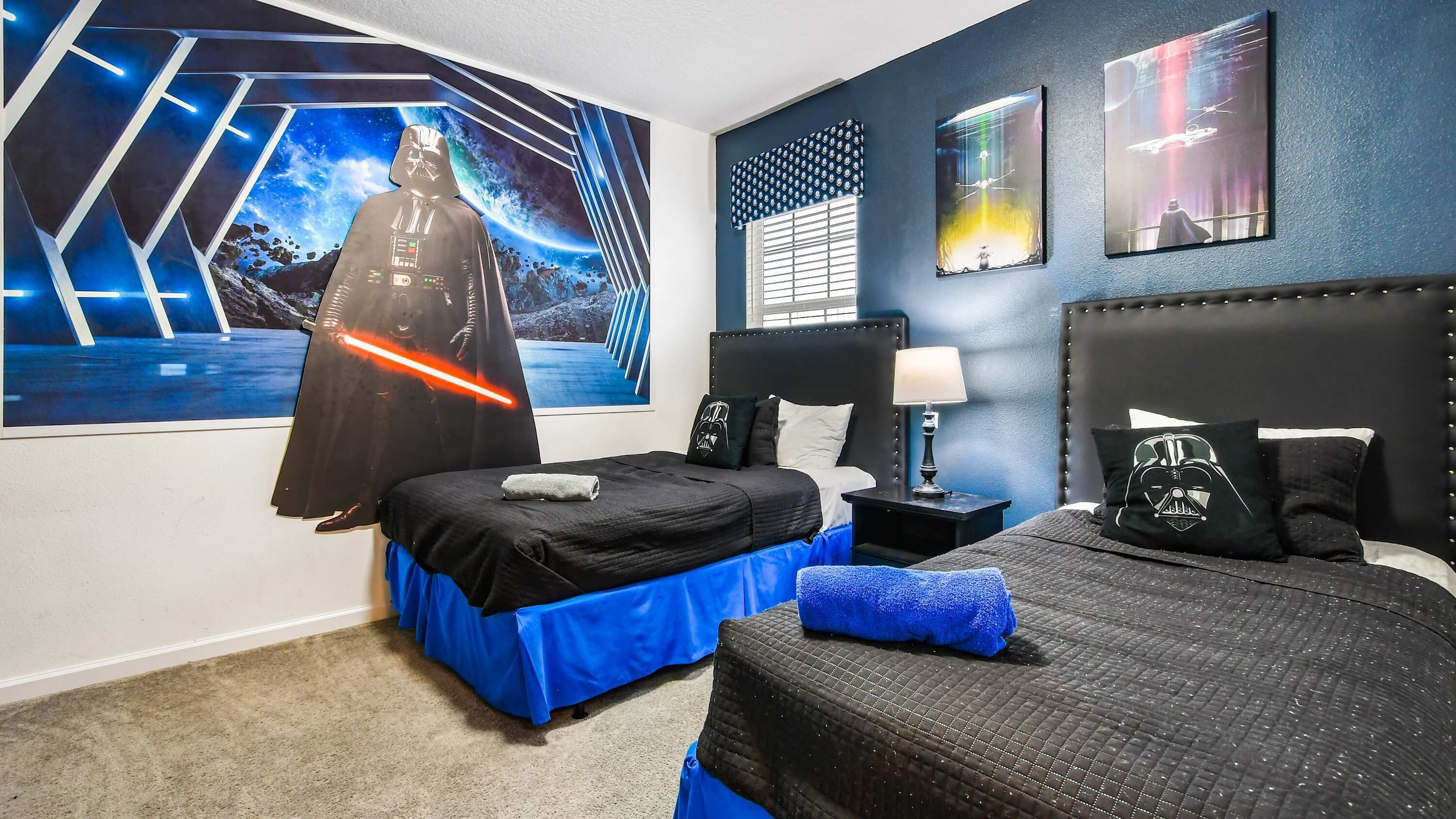 Ein Hotelzimmer mit zwei Betten, eines mit blauem Bettlaken, einem großen Darth-Vader-Poster an der Wand und Star-Wars-Kissen.