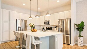 A modern kitchen with white cabinetry, stainless steel appliances, and pendant lighting. - Spacious 12-bed Villa With Pool & Resort Amenities (Kissimmee)