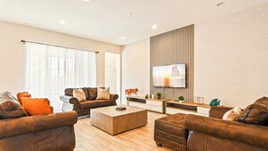 A modern living room with leather sofas, a coffee table, and a flat-screen TV mounted on a wooden panel wall. - Spacious 12-bed Villa With Pool & Resort Amenities (Kissimmee)