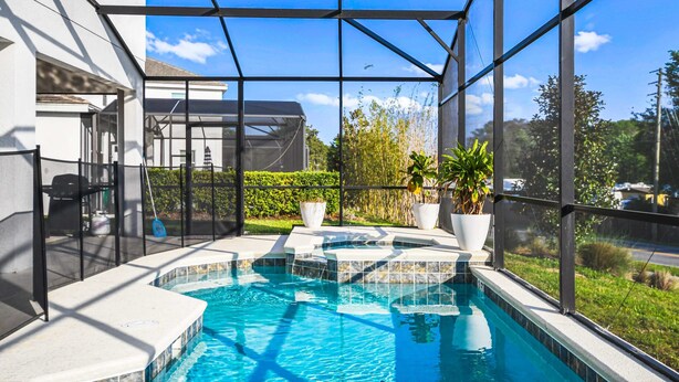 A swimming pool with a glass enclosure, surrounded by potted plants and a view of the neighborhood. - Spacious 12-bed Villa With Pool & Resort Amenities (Kissimmee)