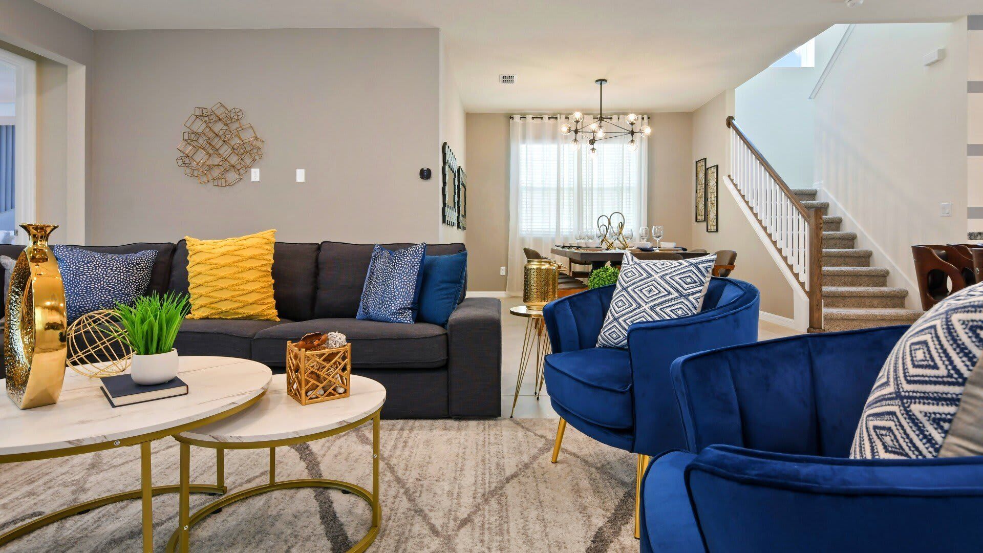A modern living room with a dark sofa, blue armchairs, a round coffee table, and a dining area in the background.