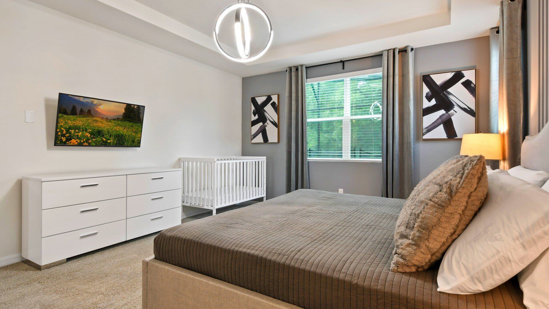 Une chambre à coucher avec un lit, une commode blanche, un berceau et des œuvres d’art accrochées aux murs.