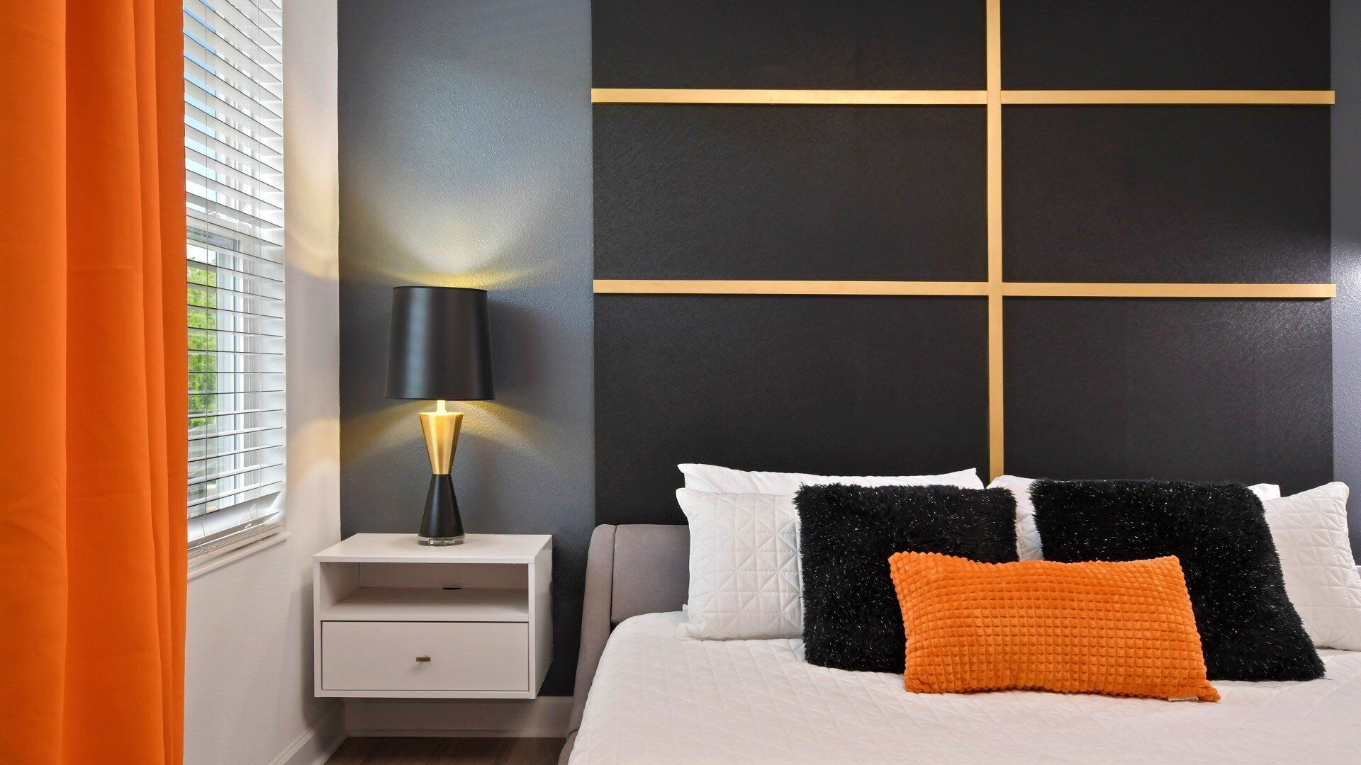 A bedroom with a bed, nightstand, lamp, and a window with blinds.