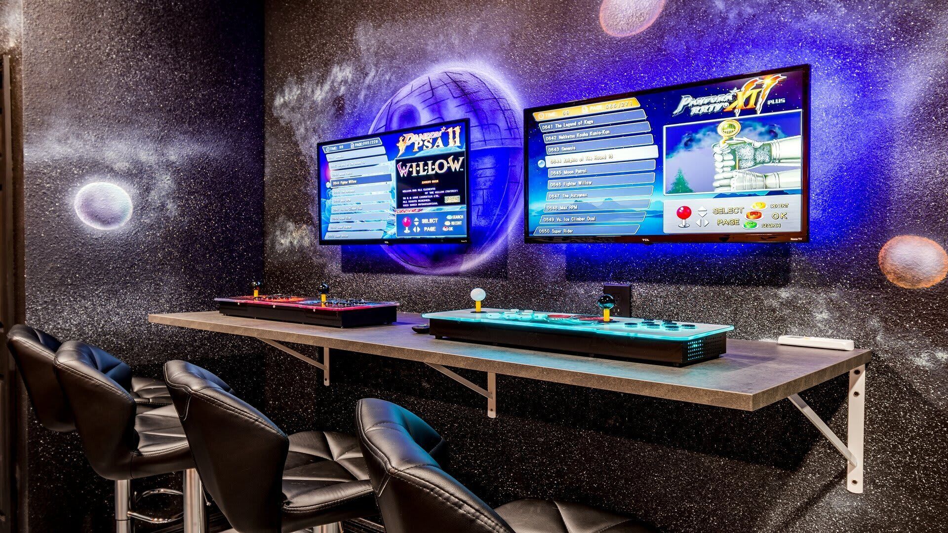 A gaming setup with two monitors displaying video games, a DJ controller, and a pool table in a room with a space-themed wall.
