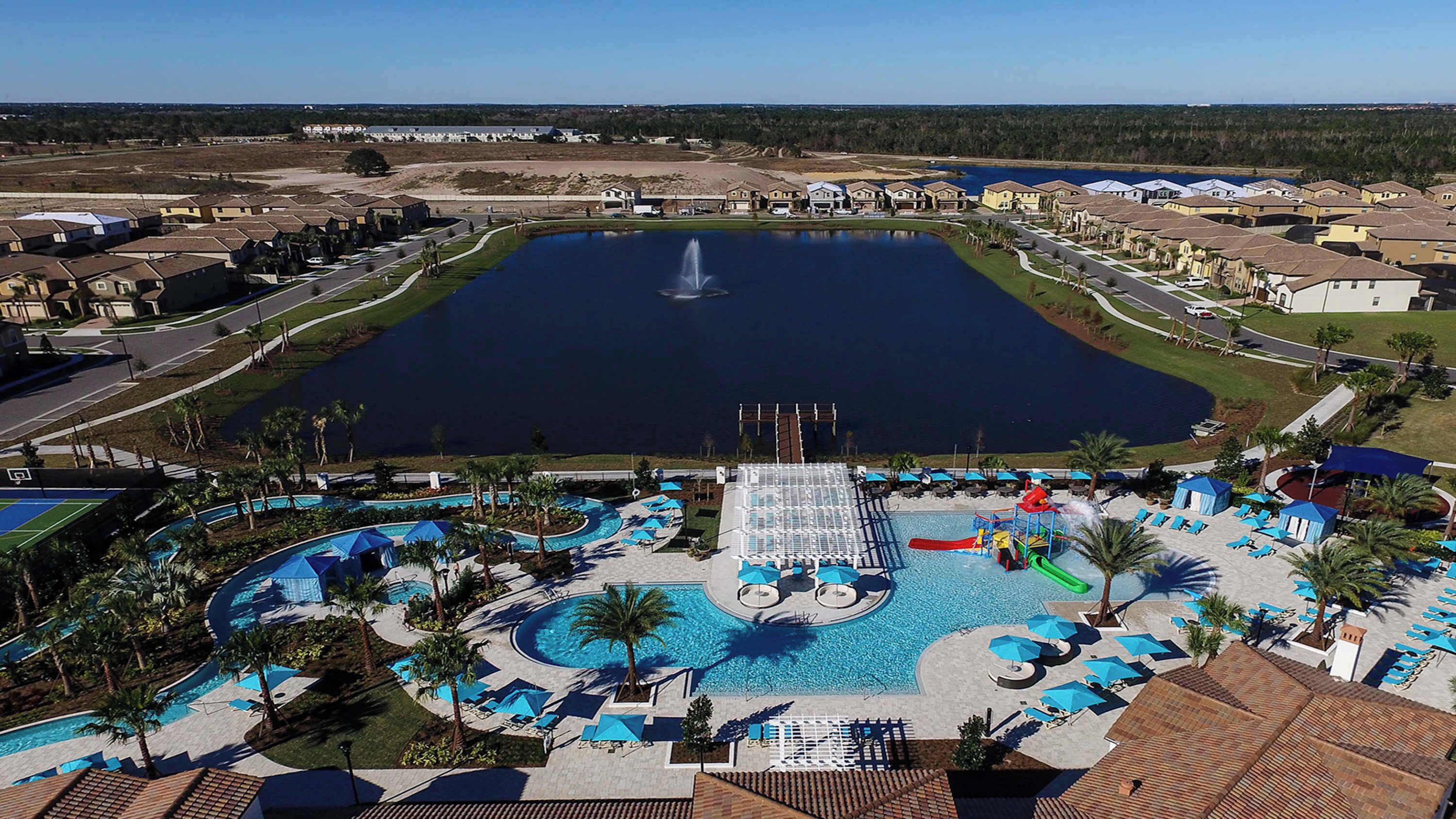 A large outdoor swimming pool with a water slide, surrounded by lounge areas and palm trees.