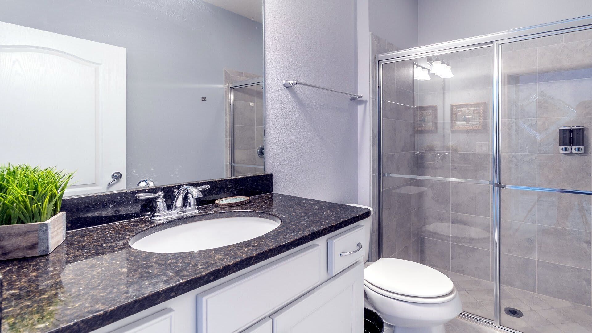 Un baño moderno con lavamanos de encimera de granito, cabina de ducha de vidrio y un inodoro blanco.