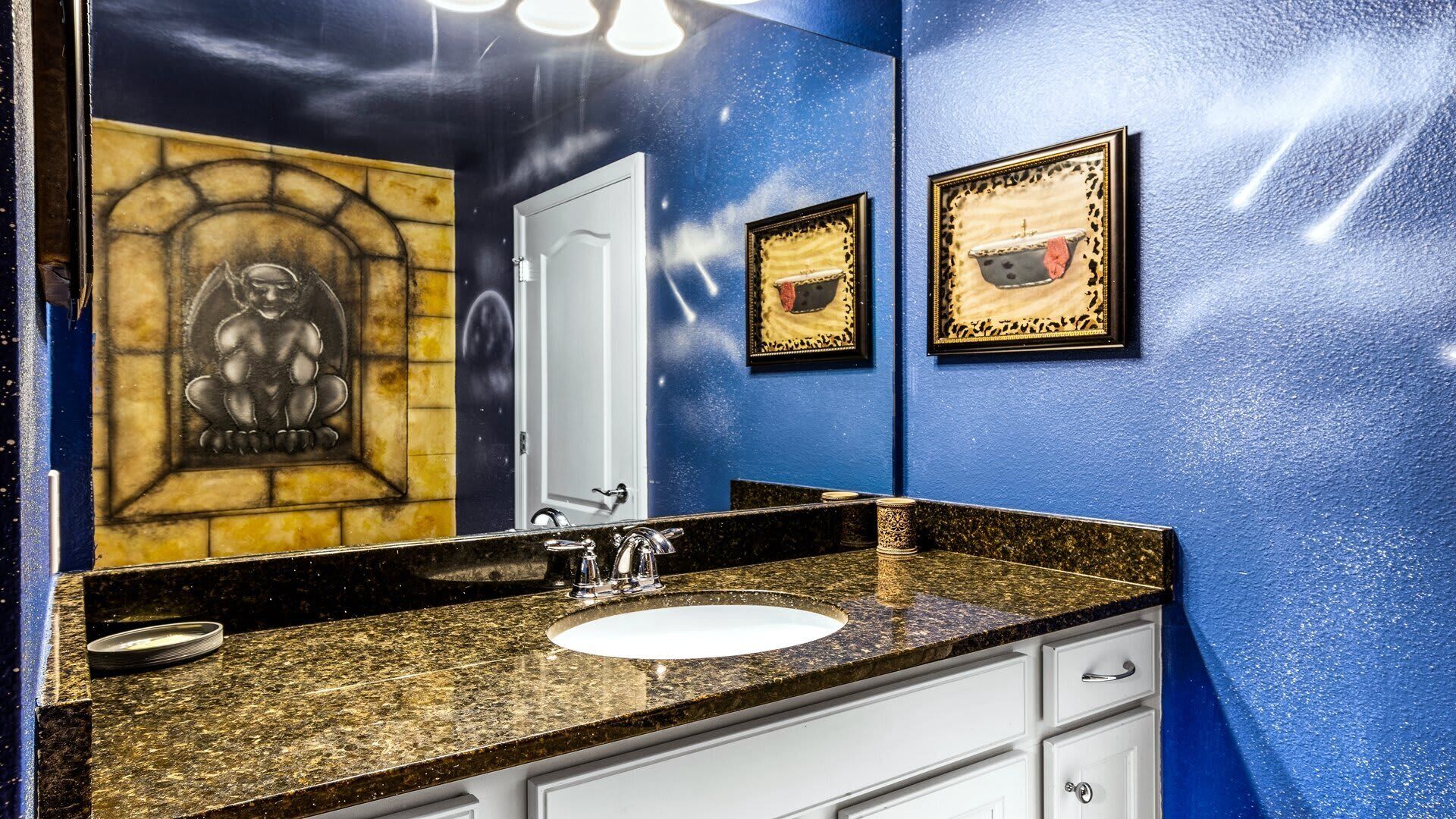A bathroom with a granite countertop, a white sink, and a mirror. There are two framed pictures on the wall.