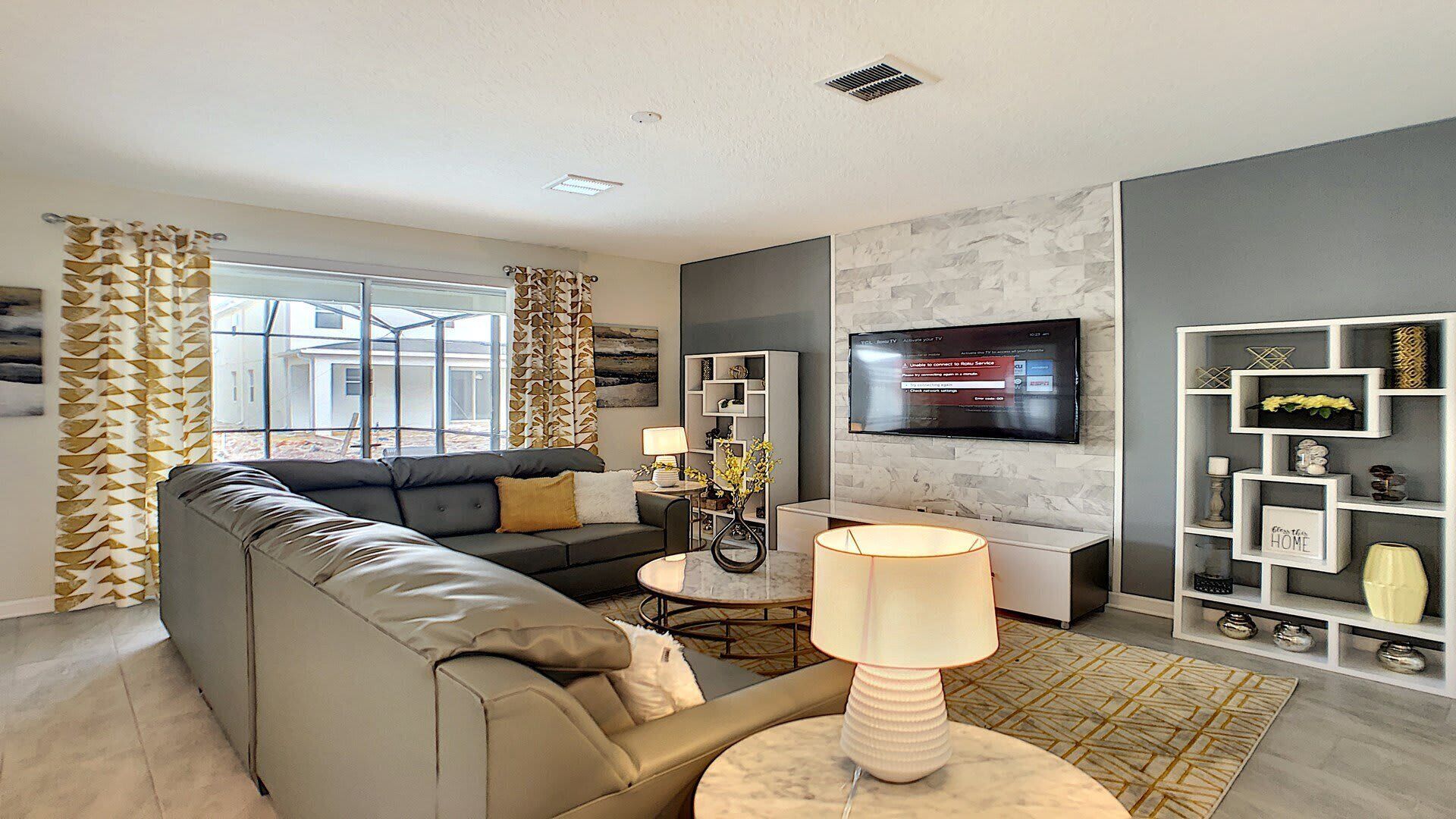 A modern living room with a sectional sofa, a TV mounted on the wall, and a decorative shelf unit.