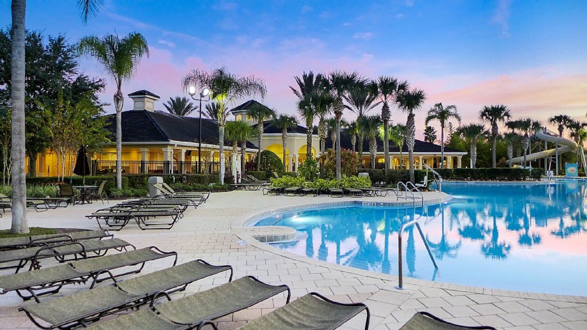 A resort pool area with lounge chairs, palm trees, and a water slide.