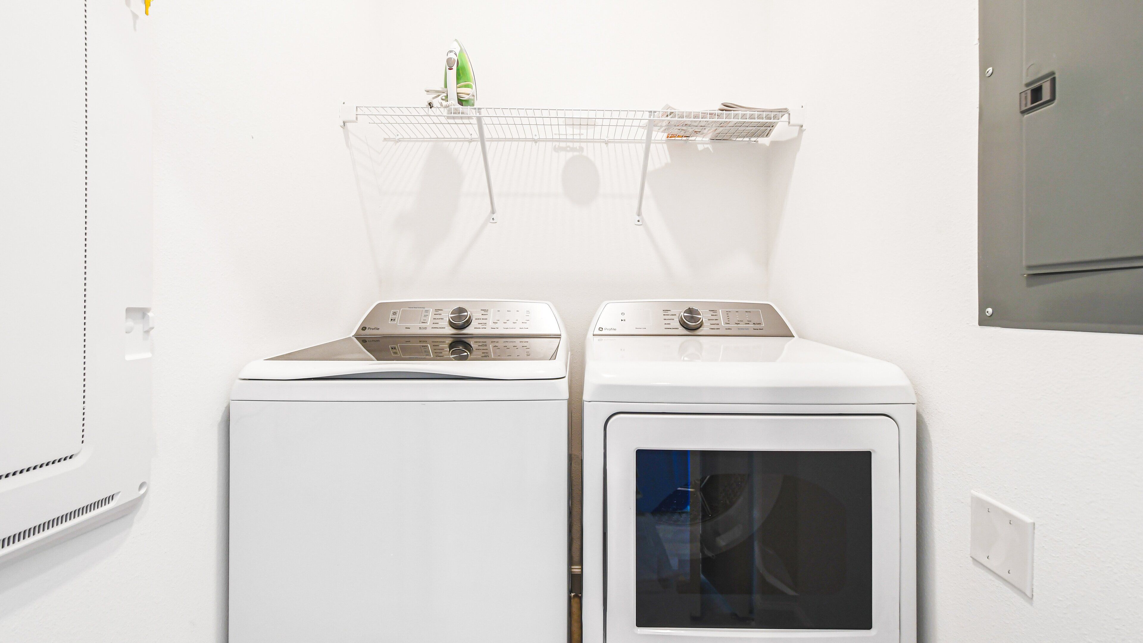 A laundry area with two front-loading washing machines and a drying rack above them.