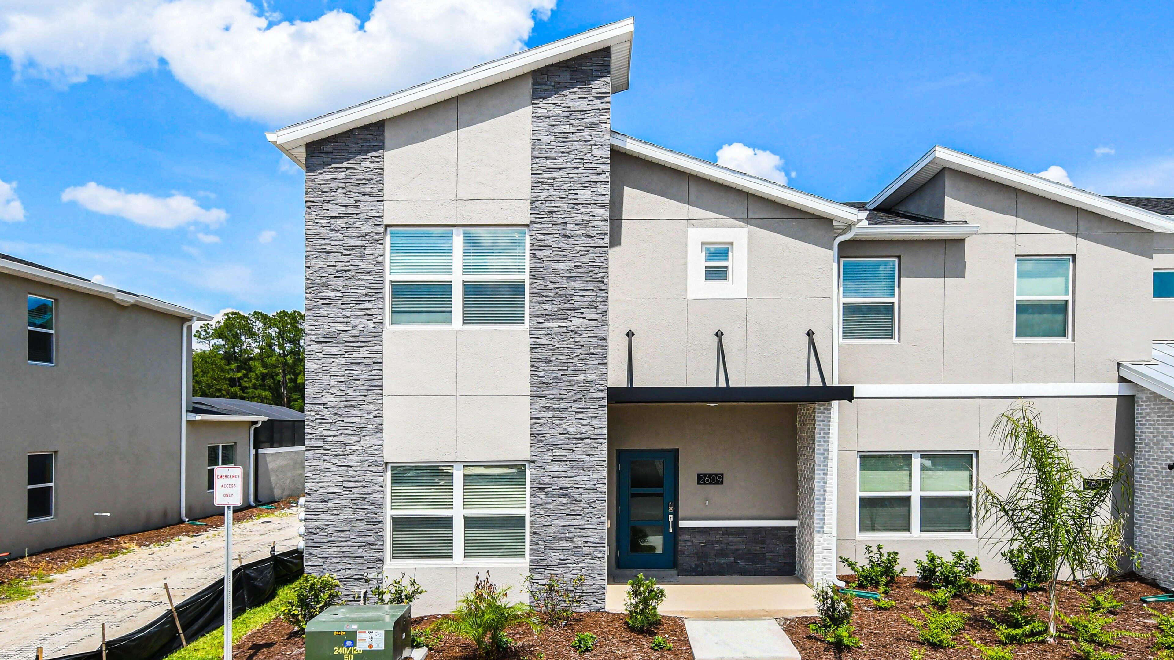 A modern two-story apartment building with a stone facade, multiple windows, and a small front porch.