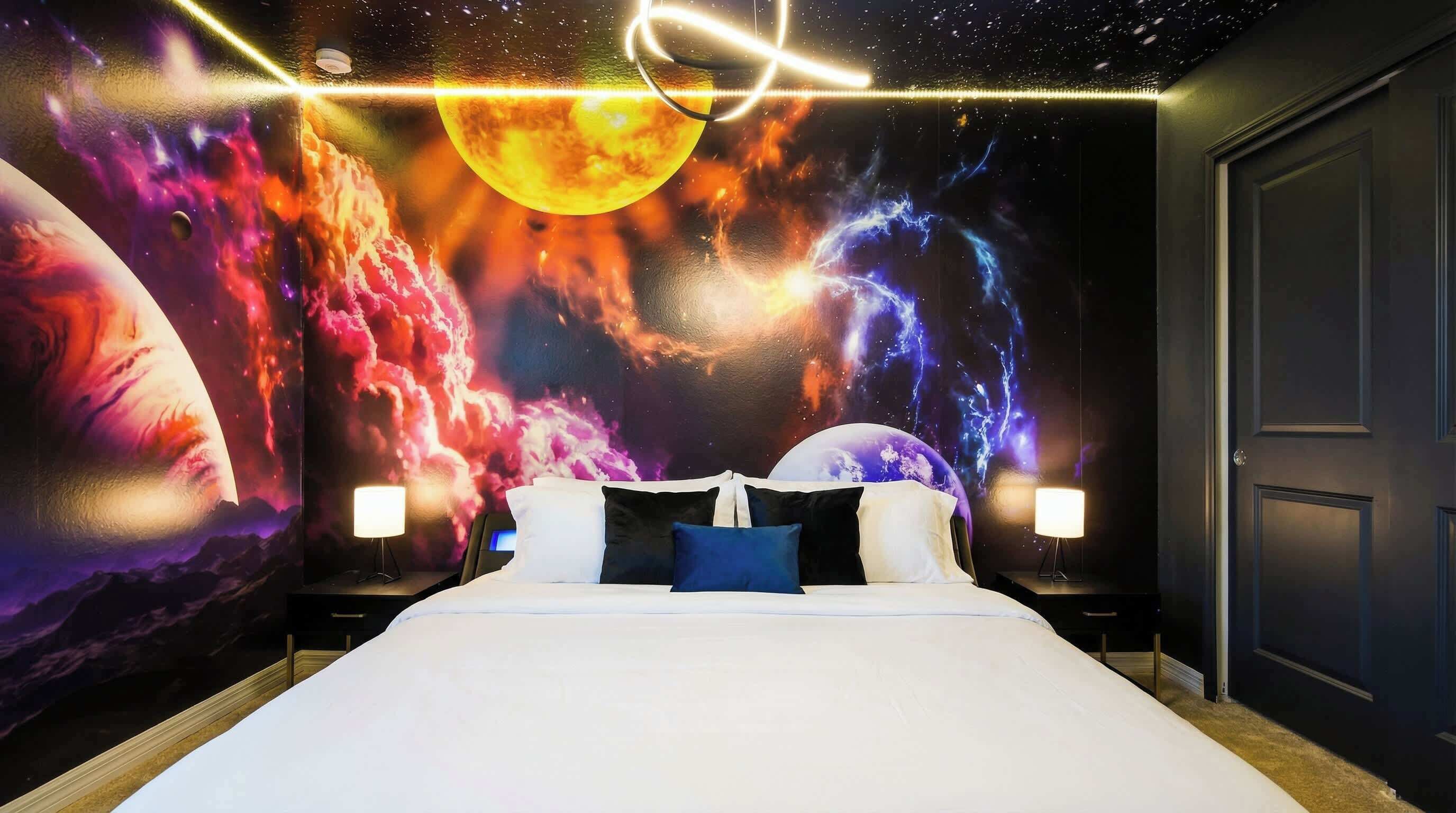 A bedroom with a bed, two bedside tables, and a wall mural of a cosmic scene.
