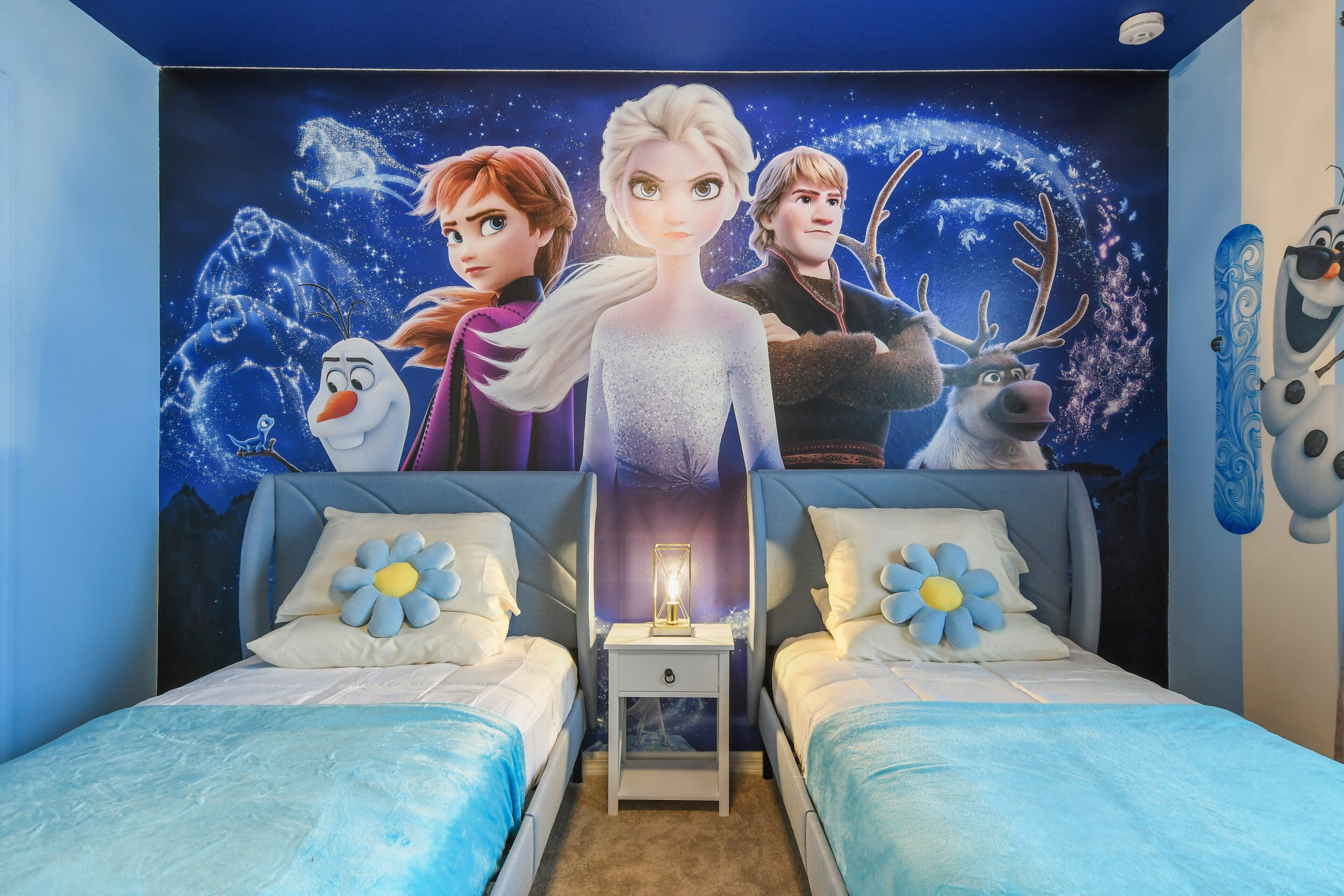 A bedroom with two beds, a nightstand, and a wall mural of animated characters.