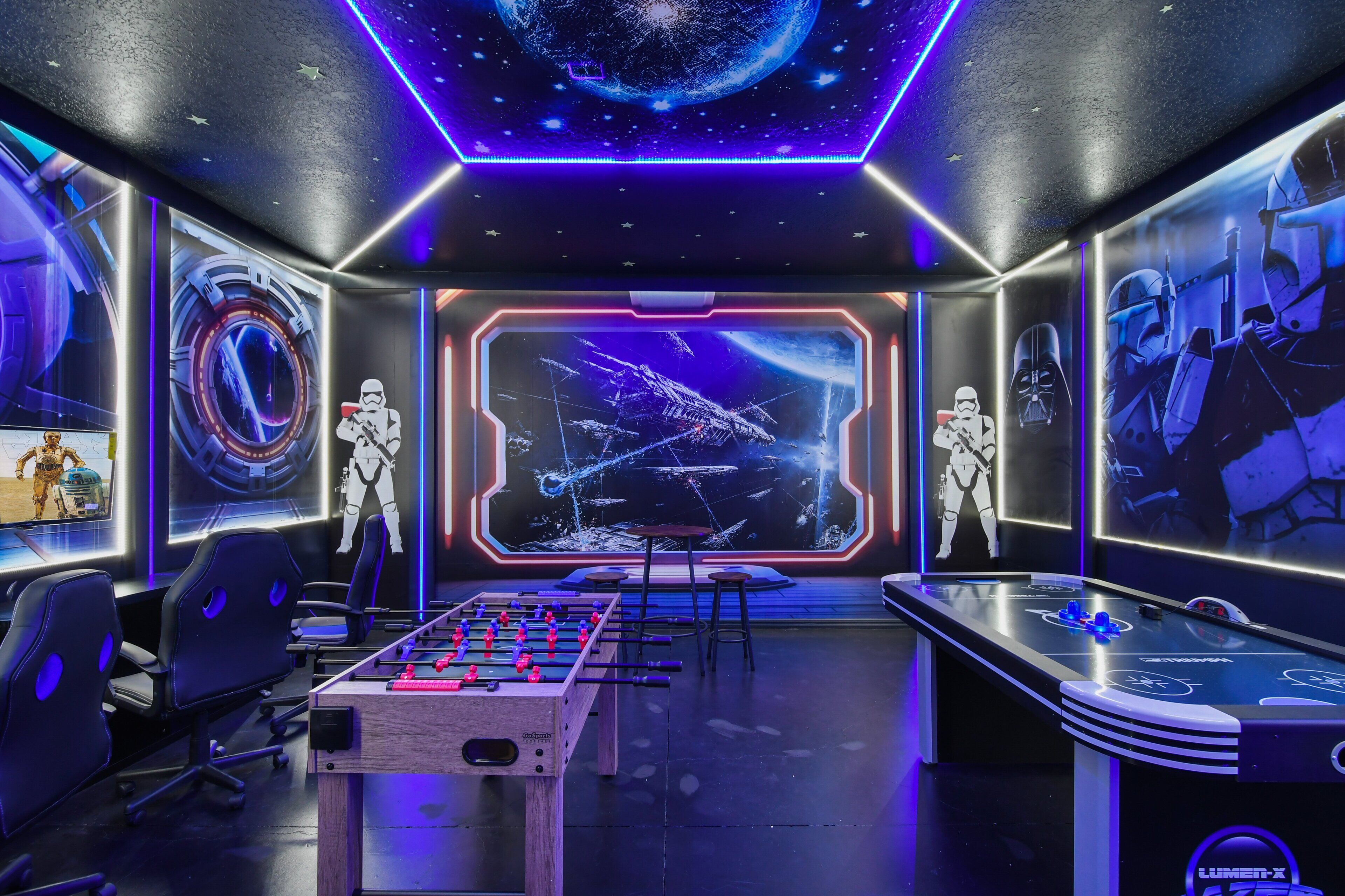 A room with a foosball table, Star Wars-themed decor, and a large screen displaying space scenes.