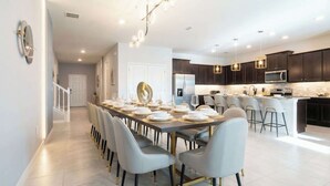 A modern kitchen with dark cabinets, a central island, and a dining area with a long table and chairs. - Luxury Family Escape at Windsor Island Orlando (Davenport)