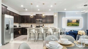 A modern kitchen with dark cabinets, stainless steel appliances, and a central island with bar stools. - Luxury Family Escape at Windsor Island Orlando (Davenport)
