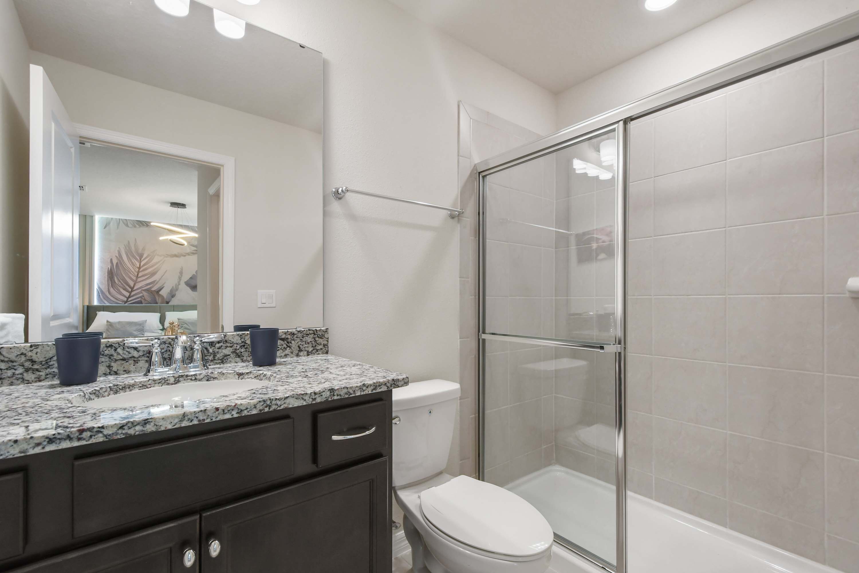 Une salle de bain avec une douche à parois de verre, des toilettes blanches et un comptoir en granit surmonté d’un miroir.