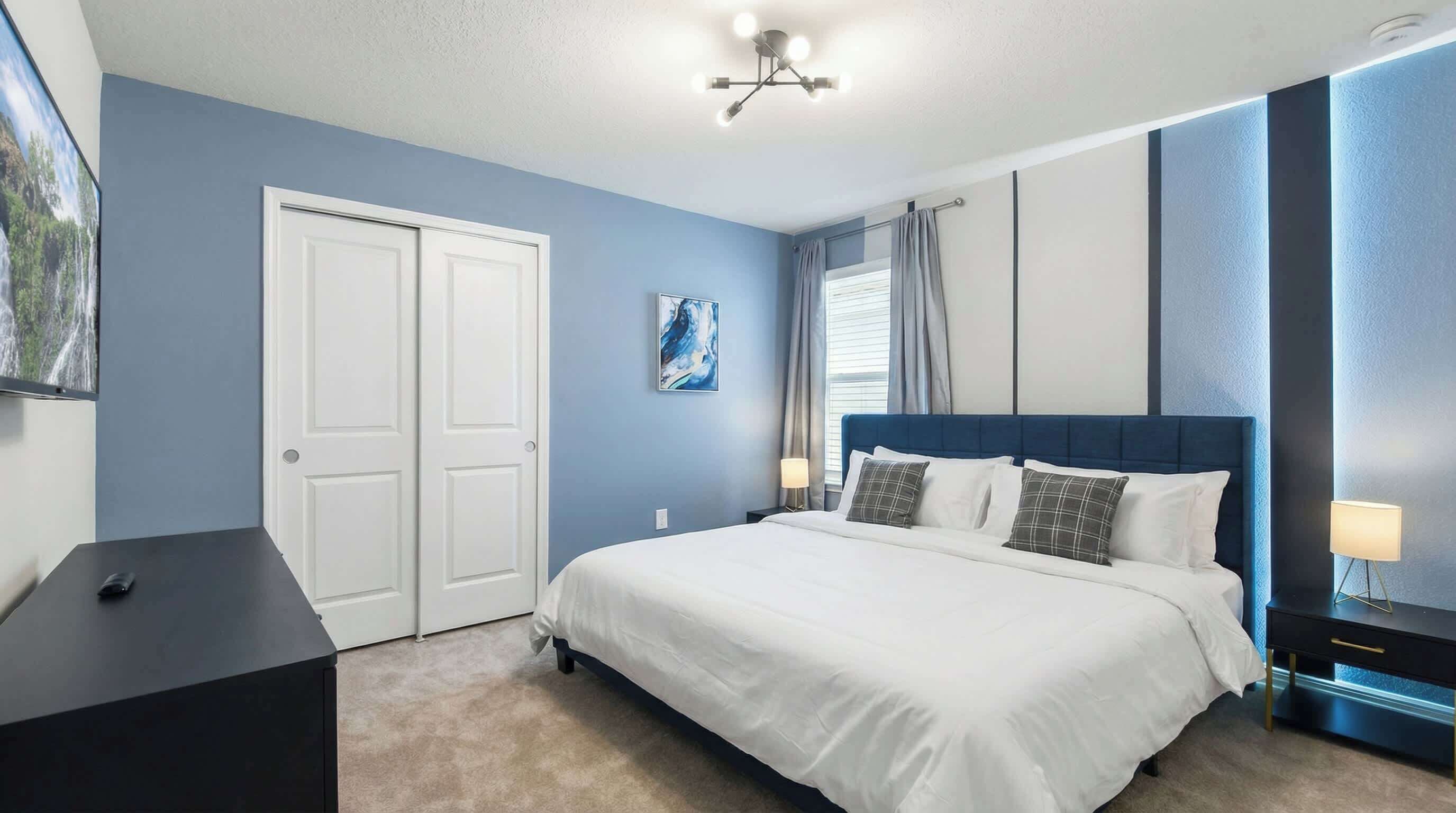 Een slaapkamer met een bed, een bureau, een stoel, een kledingkast en een schilderij aan de muur.