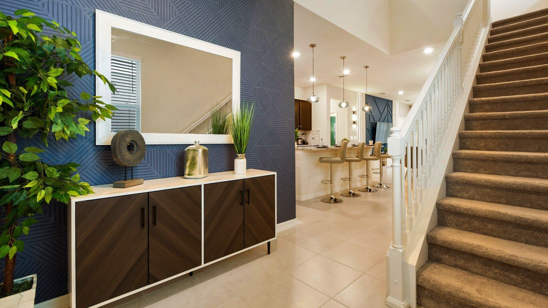 A modern kitchen with a central island, a staircase, and a dining area with bar stools.