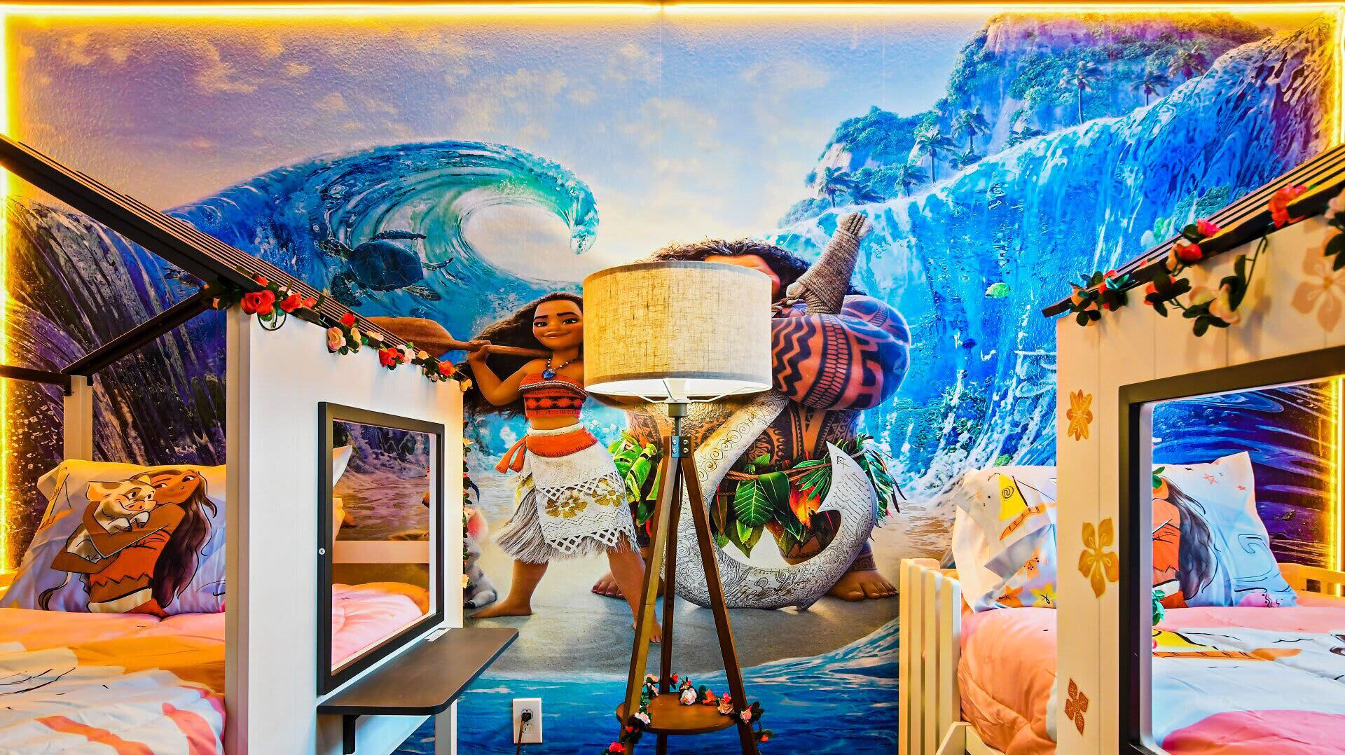 Una habitación con un mural de cascada tropical, una cama con colcha rosa y blanca, y una mesita con una lámpara.