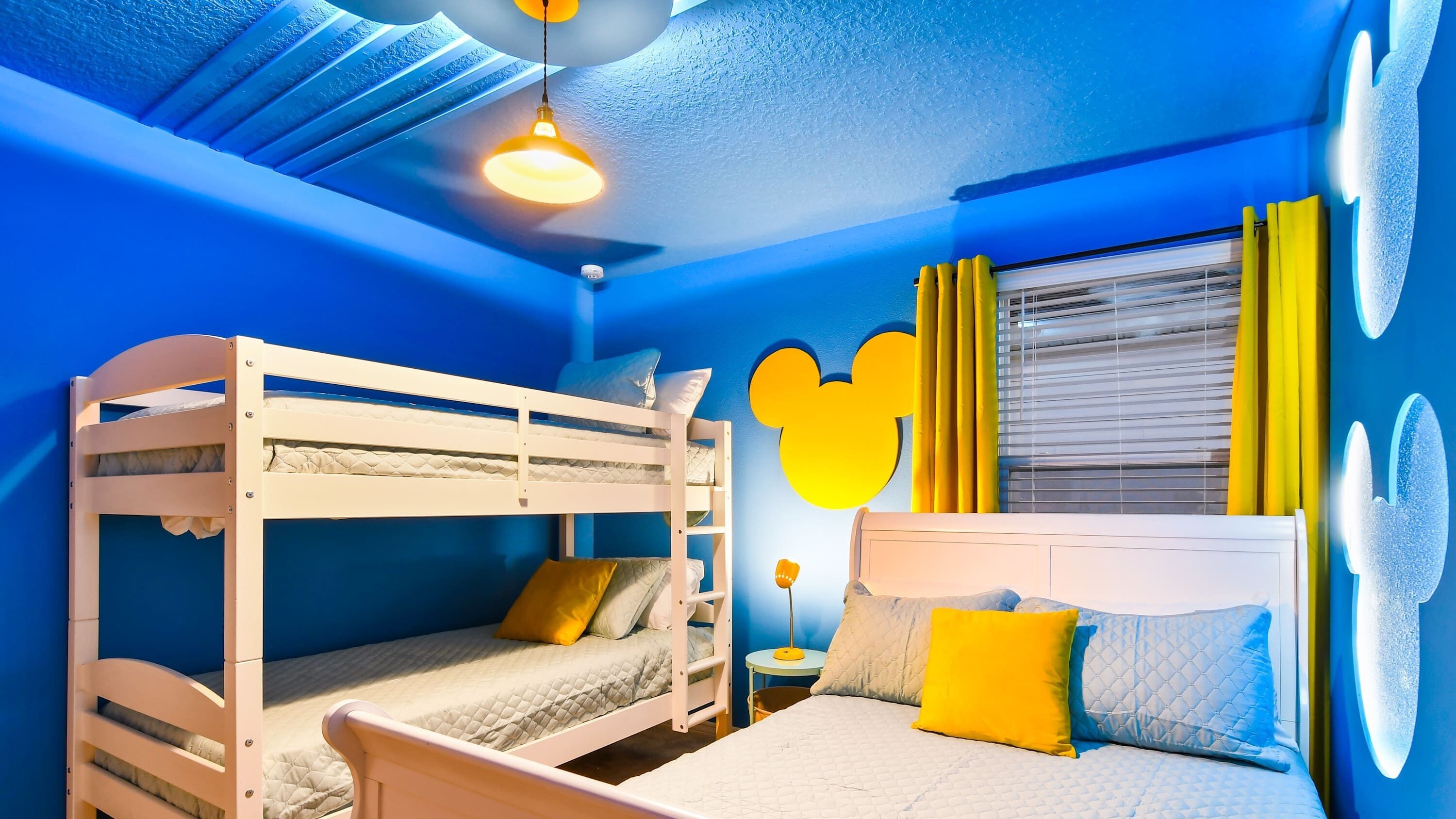 Une chambre avec un lit superposé, une fenêtre, une table de chevet et une décoration à l’effigie de Mickey Mouse.