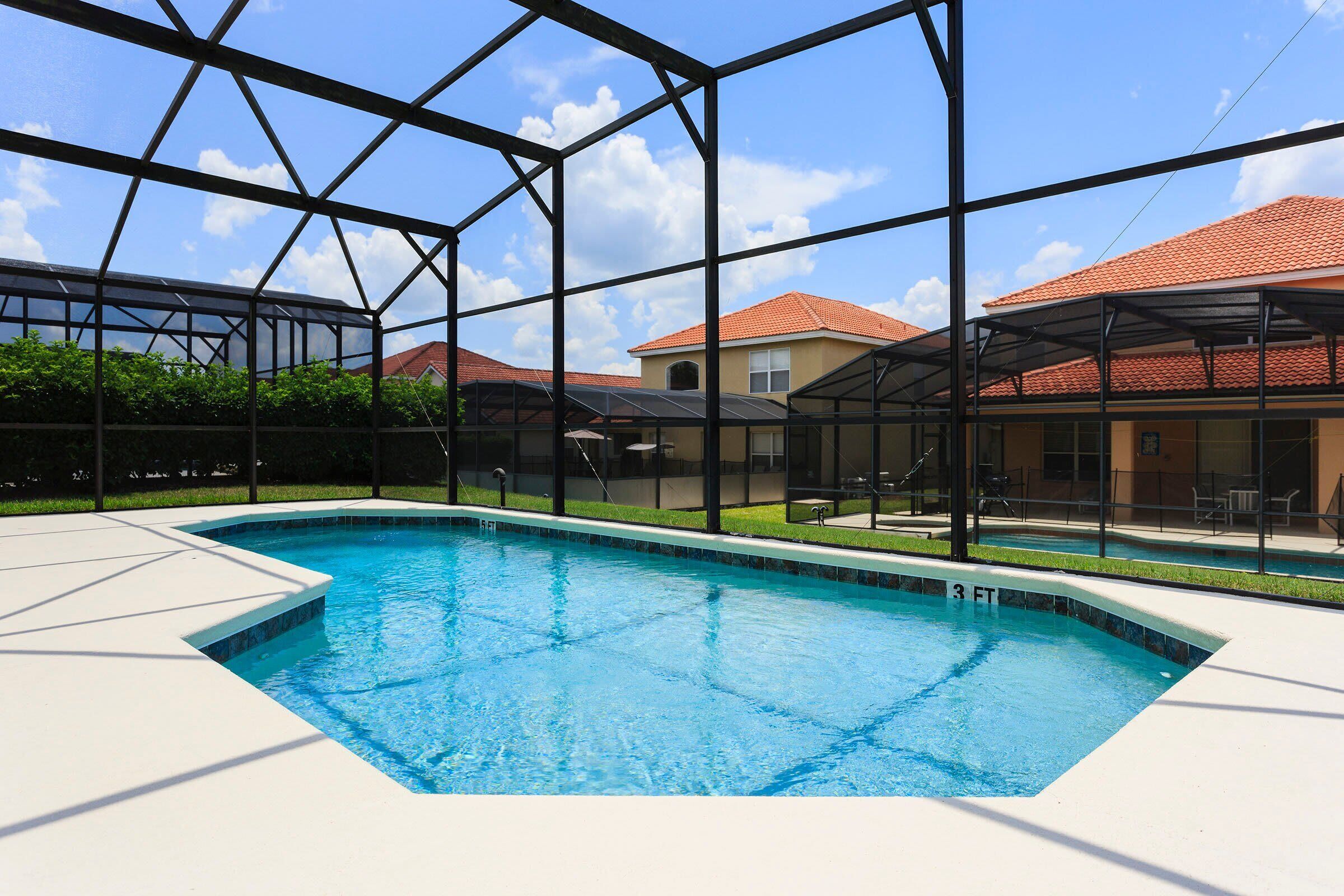 Una piscina con agua cristalina azul, rodeada por un recinto de vidrio y con vistas a casas al fondo.