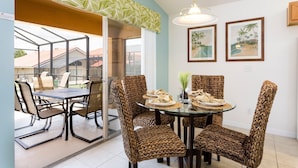 Uma sala de jantar com uma mesa de vidro, cadeiras de fibra natural, um lustre e quadros nas paredes.
