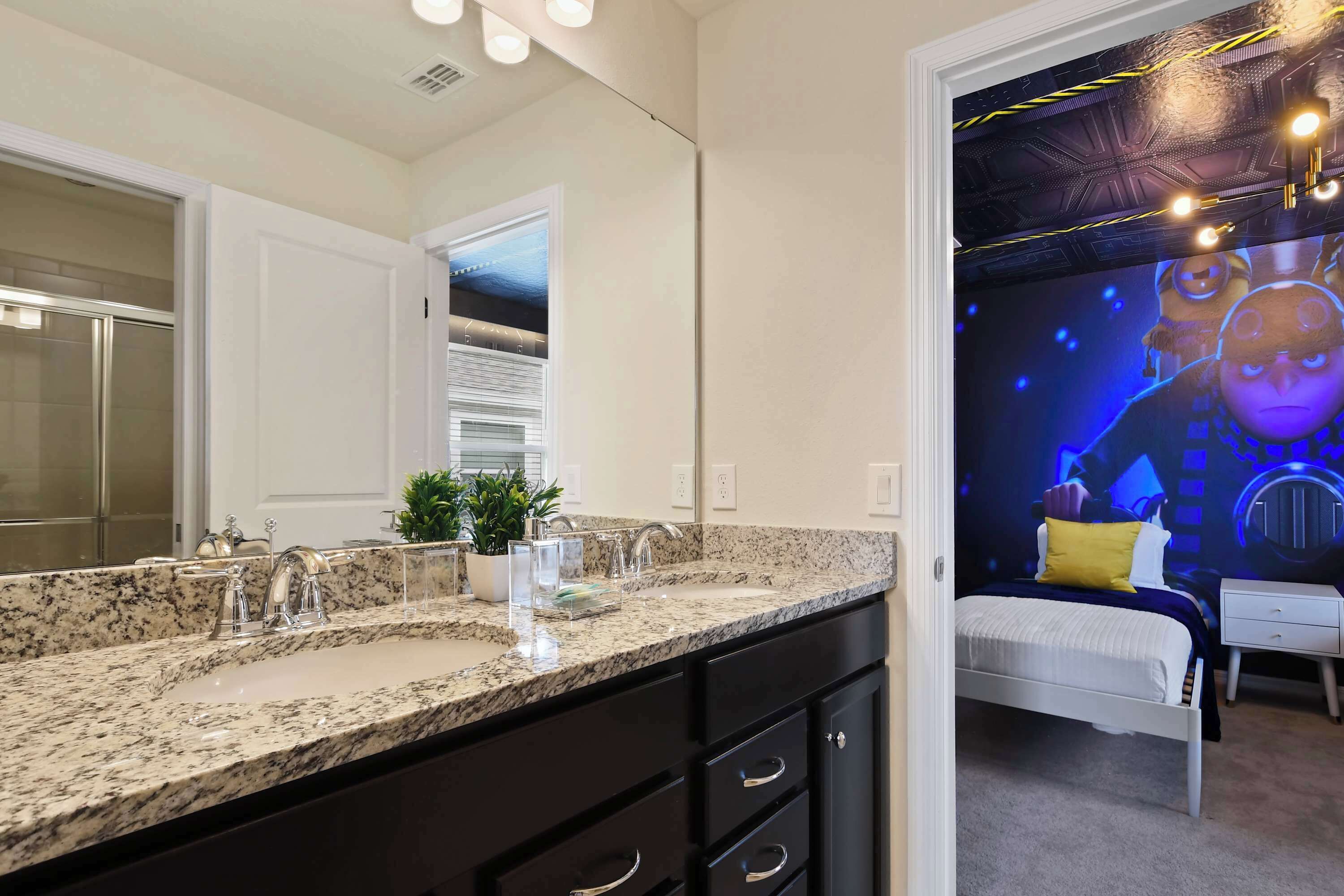 Un baño moderno con encimera de granito, un espejo grande y una puerta blanca que da a un dormitorio.
