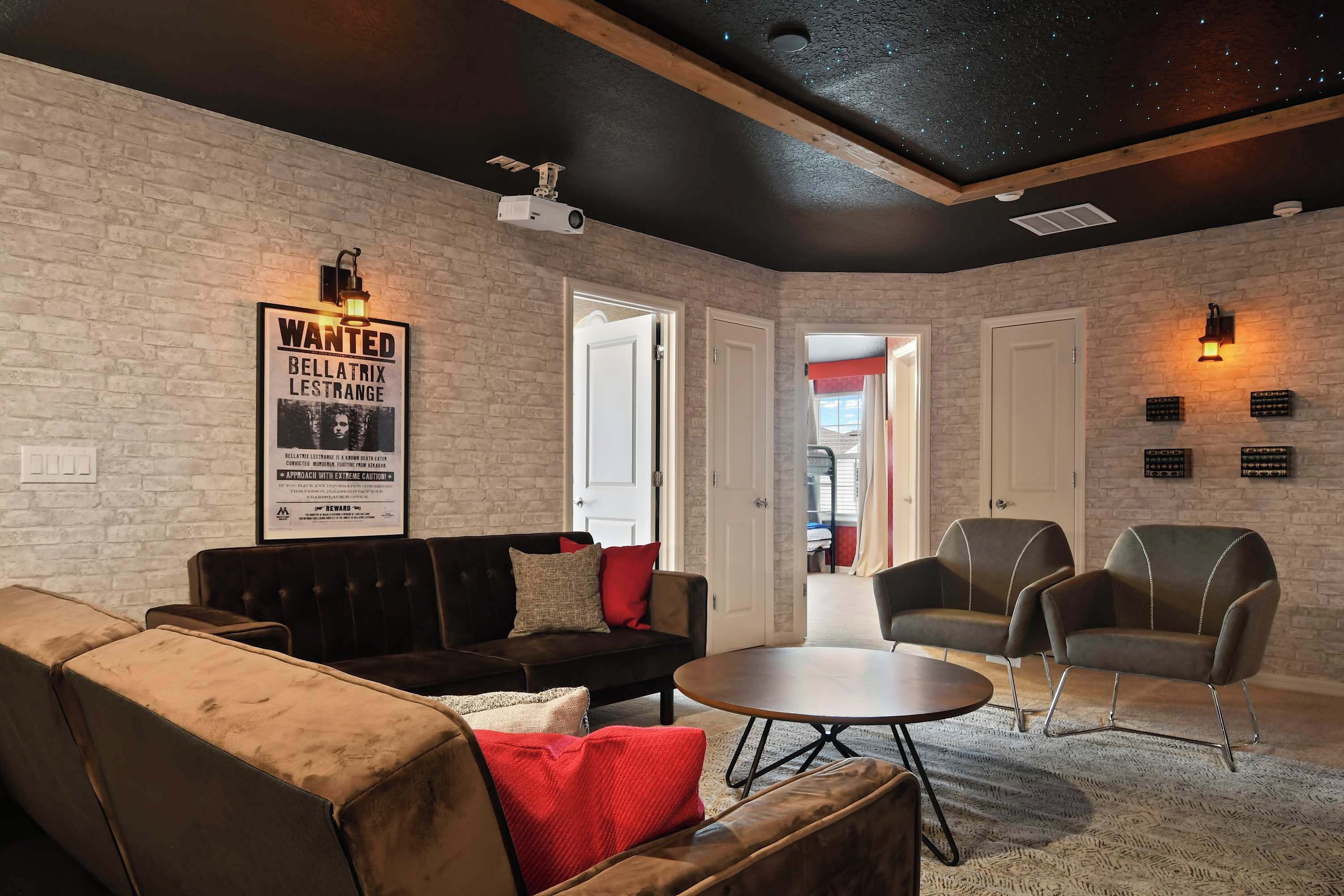 Ein gemütliches Wohnzimmer mit Backsteinwand, einem 'Wanted'-Poster, einem dunkelbraunen Sofa, einem runden Couchtisch und zwei modernen Sesseln.