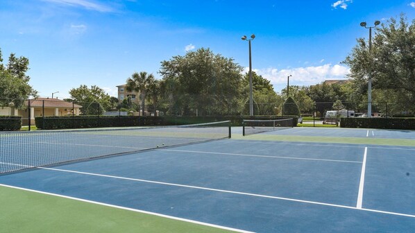 A tennis court with a net, surrounded by trees and buildings.