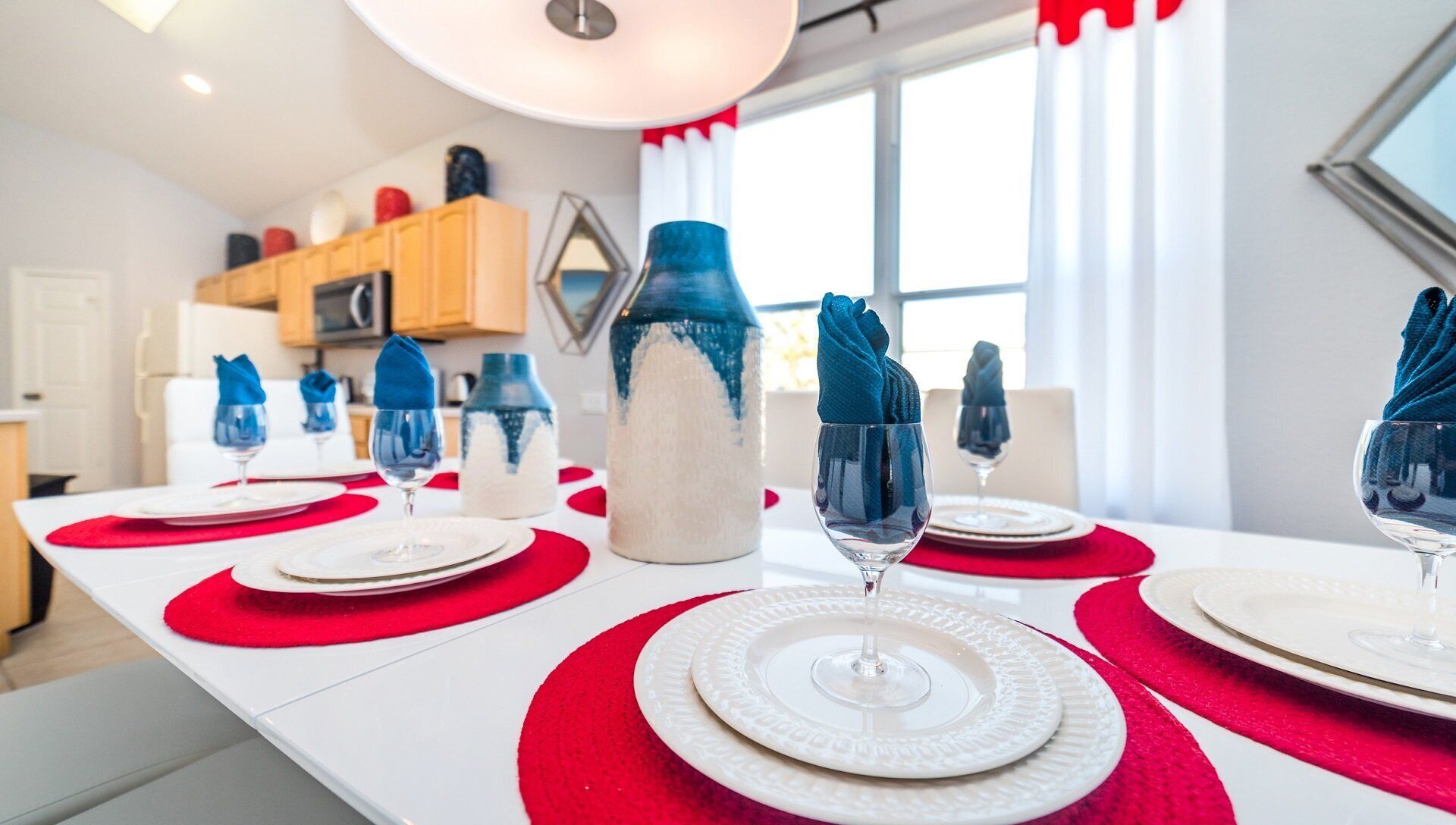 A dining table set with white plates, red placemats, and blue napkins.