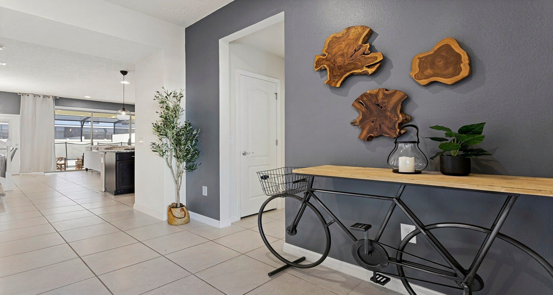 A modern kitchen with a grey accent wall, wooden art pieces, a bicycle, and a potted plant.