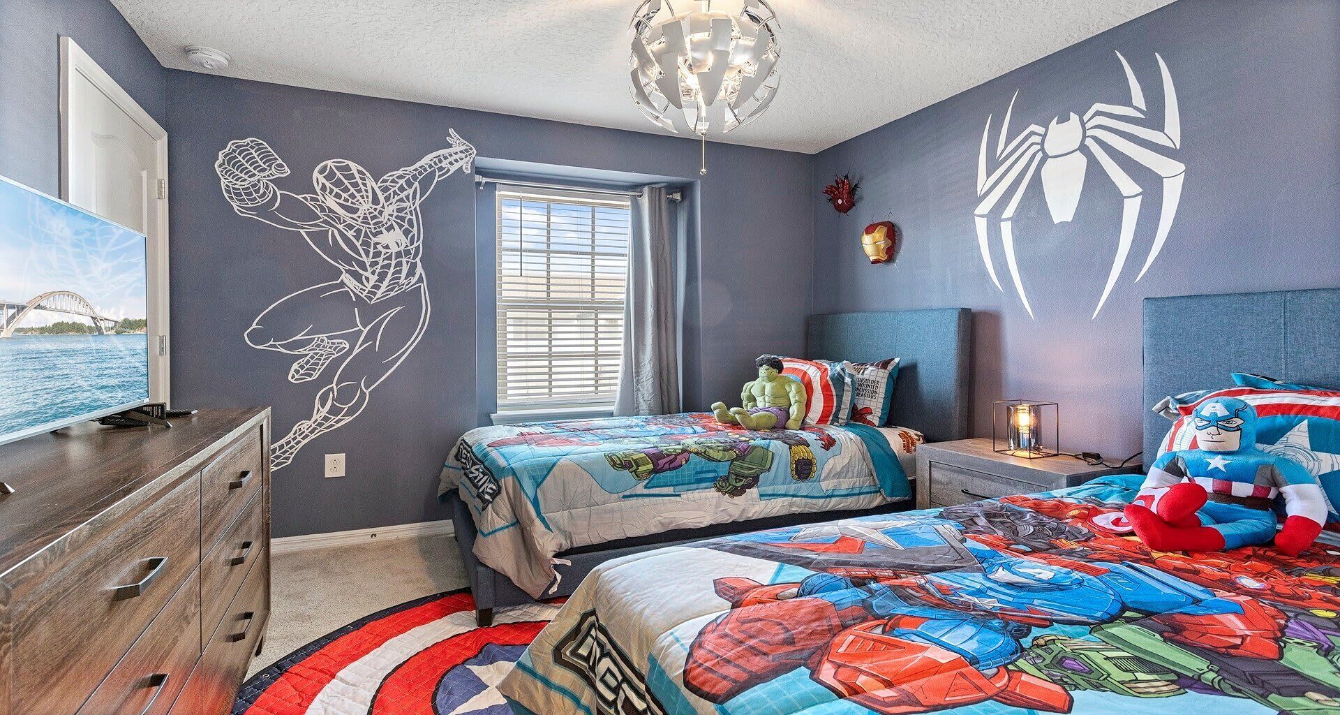 A bedroom with two beds, a TV, and wall art featuring superhero characters.