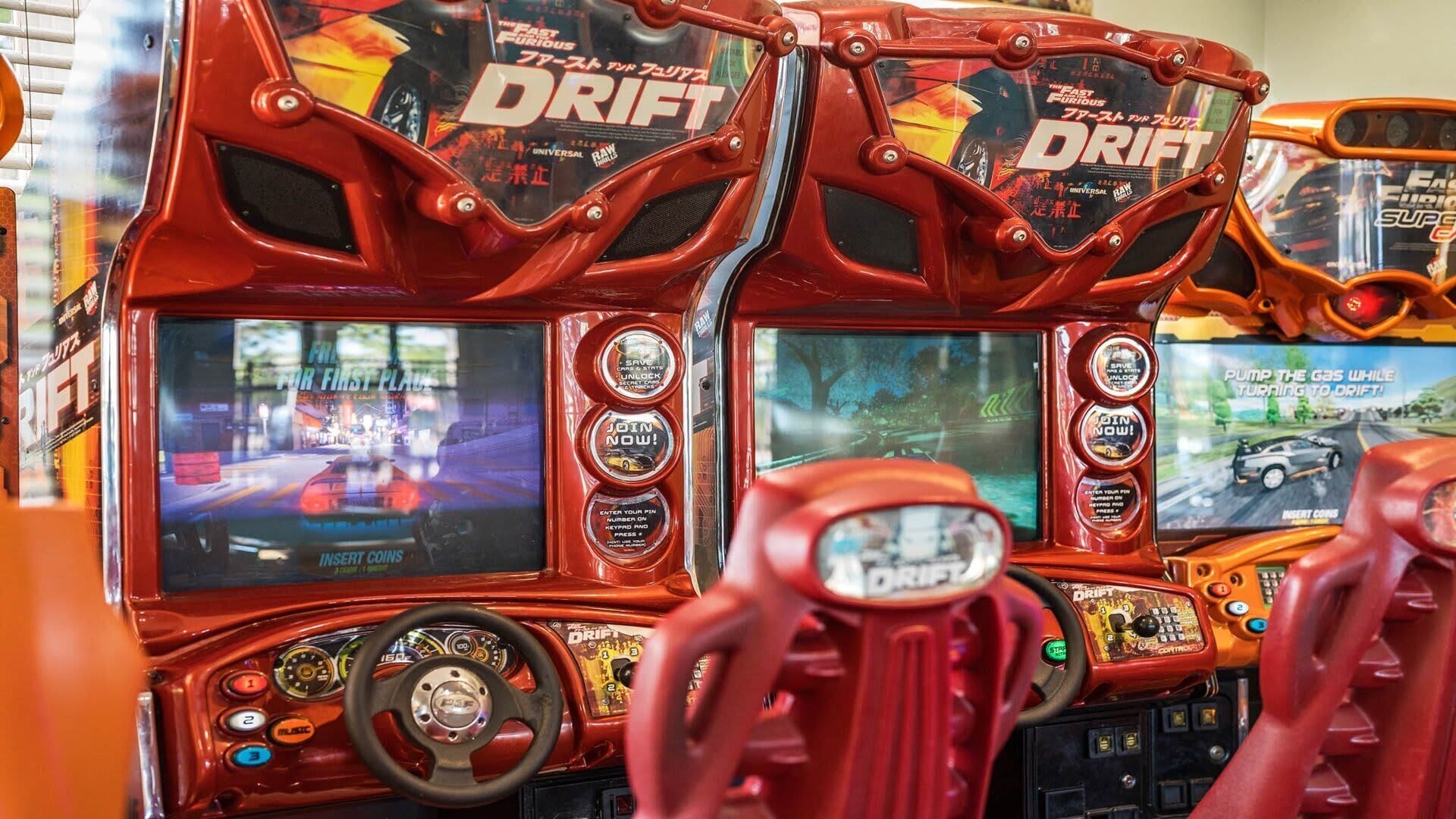 A red arcade racing game machine with multiple screens and control buttons.