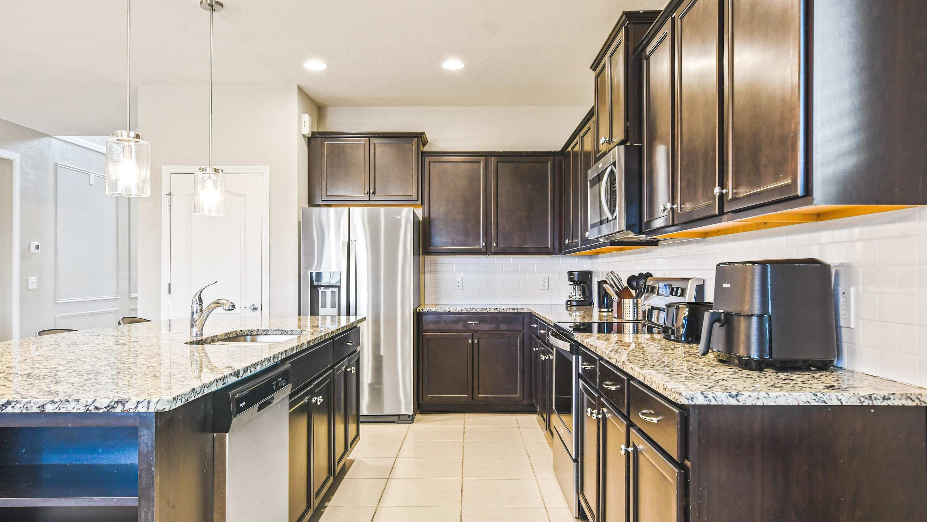 A modern kitchen with dark wood cabinets, stainless steel appliances, granite countertops, and pendant lighting.