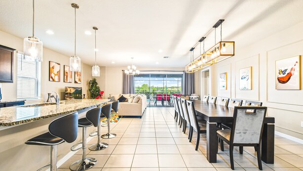 Une cuisine moderne avec une longue table à manger, des tabourets de bar et des luminaires suspendus.