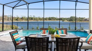 Un espace extérieur abrité comprenant une piscine, une table à manger et des chaises, avec vue sur un lac.