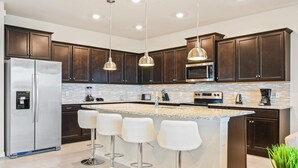 A modern kitchen with dark wood cabinets, stainless steel appliances, a granite island with bar stools, and pendant lighting. - Opulent Villa in Resort Near Theme Parks & Shops (Davenport)
