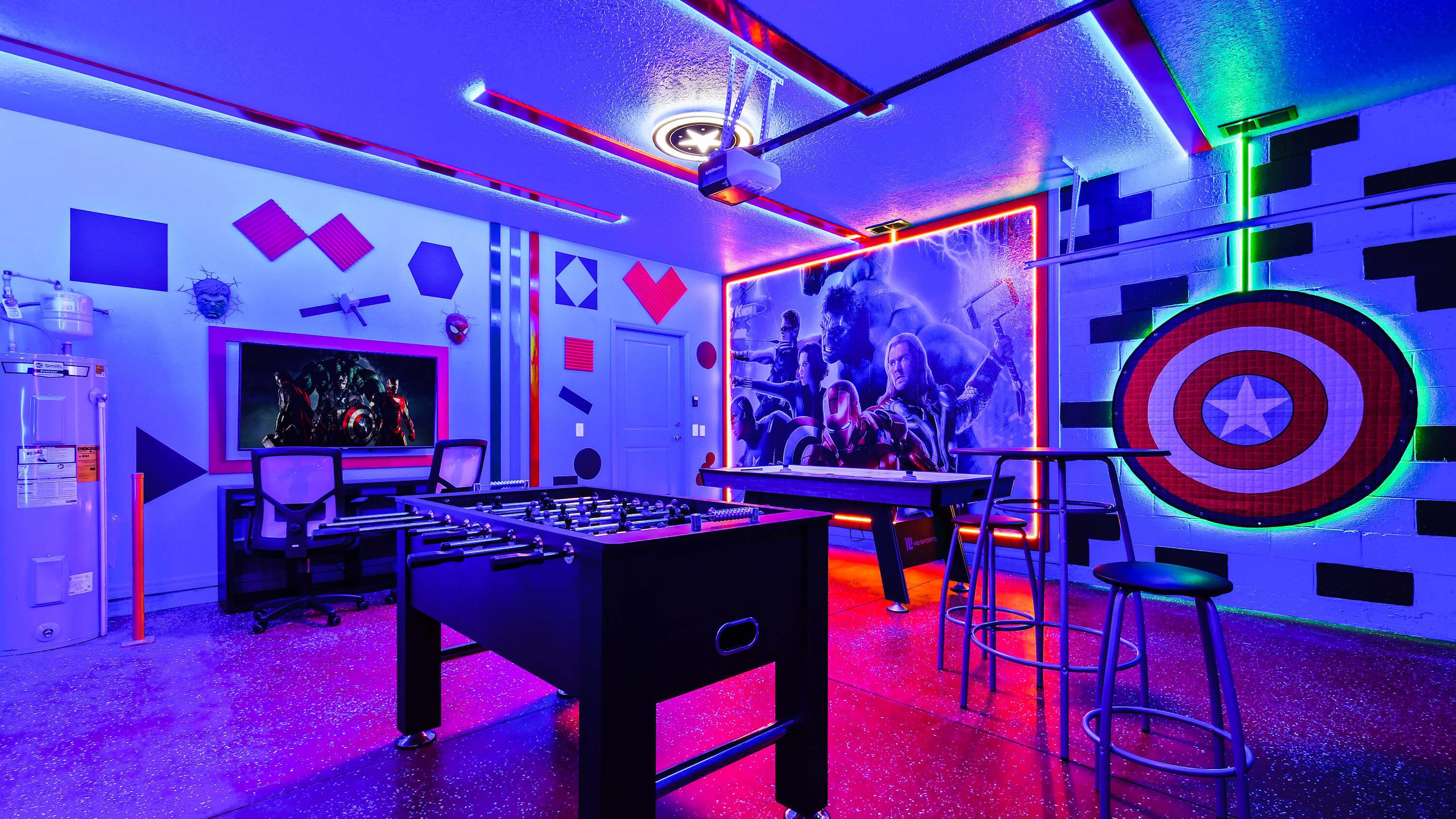 Ein Raum mit einer Fußballtischkicker, einer Projektionsleinwand und einer Wand mit Superhelden-Dekorationen.