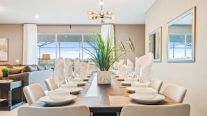 A dining room with a long table set for a meal, featuring white plates, glasses, and a central decorative plant. - Opulent Villa in Resort Near Theme Parks & Shops (Davenport)