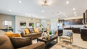A modern living room with a sofa, coffee table, and dining area. There is a kitchen with dark cabinets and a countertop. - Opulent Villa in Resort Near Theme Parks & Shops (Davenport)