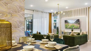 Ein modernes Wohnzimmer mit Essbereich, ausgestattet mit einer Sofagarnitur, einem an der Wand montierten Fernseher und einer dekorativen Wandverkleidung.