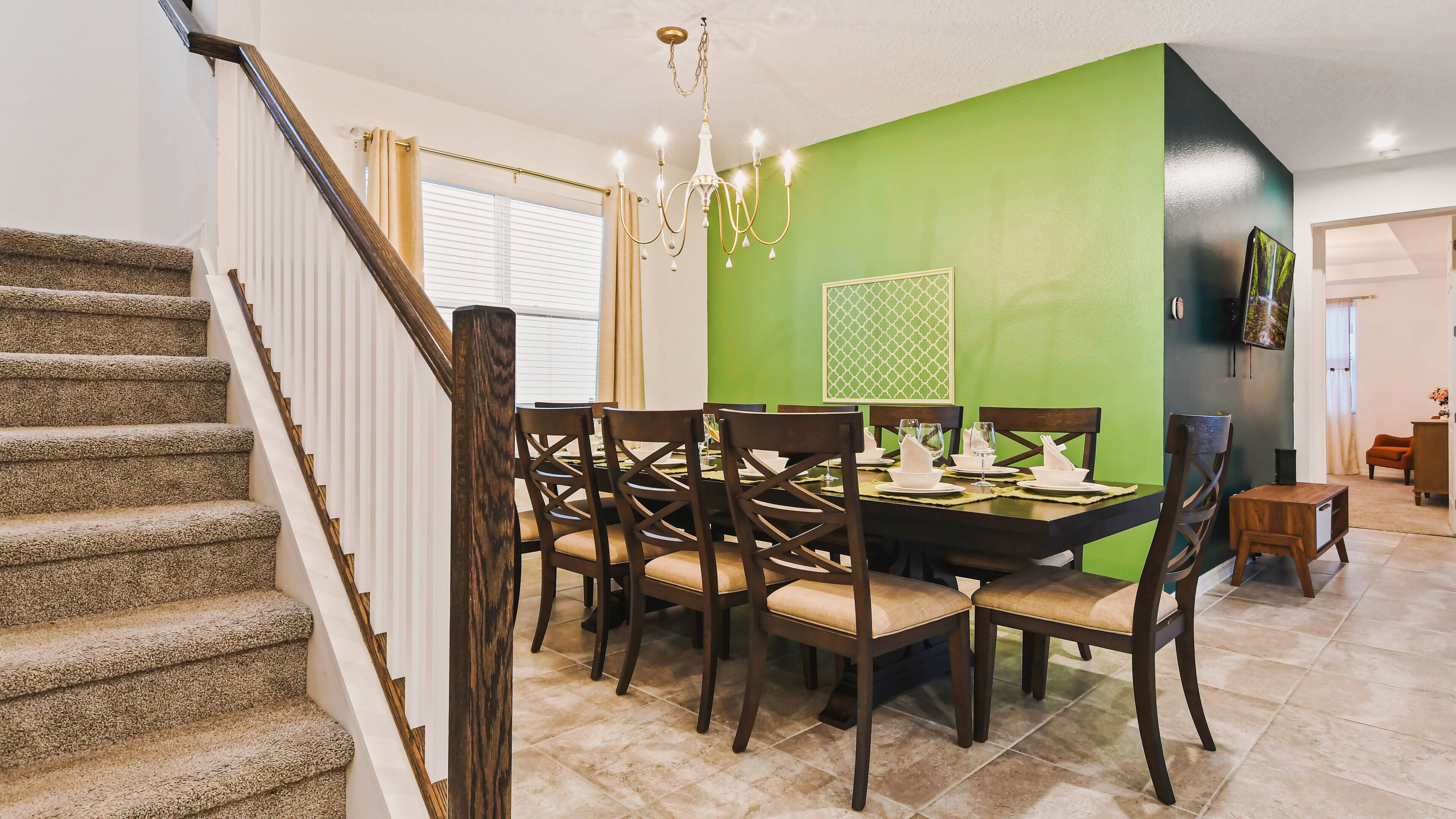 Un área de comedor con una pared de acento verde, una araña y una escalera con barandillas de madera.