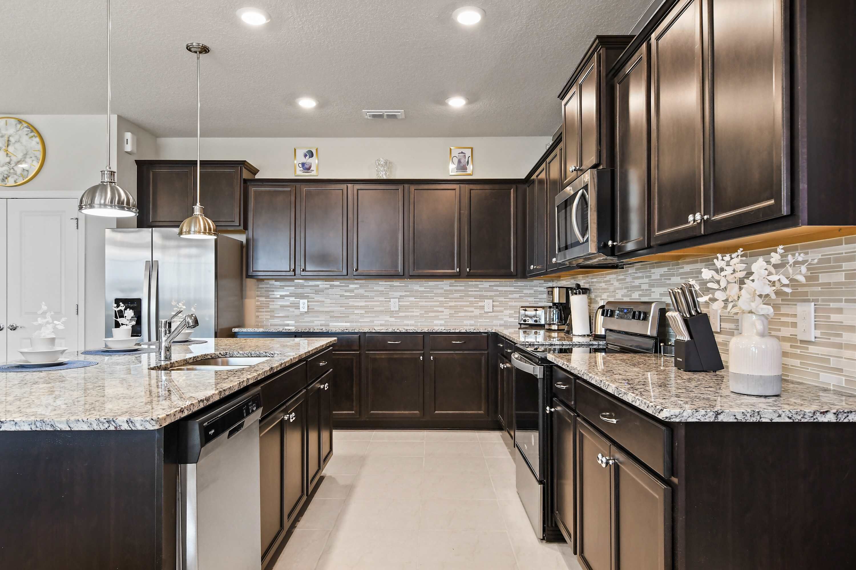 A modern kitchen with dark cabinetry, granite countertops, stainless steel appliances, and pendant lighting.
