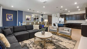 Una sala moderna con un sofá modular, una mesa de centro redonda y un comedor con sillas, y una cocina al fondo.