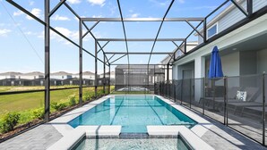 Una piscina con cerramiento de vidrio, rodeada por una zona de patio con vistas a un barrio residencial.