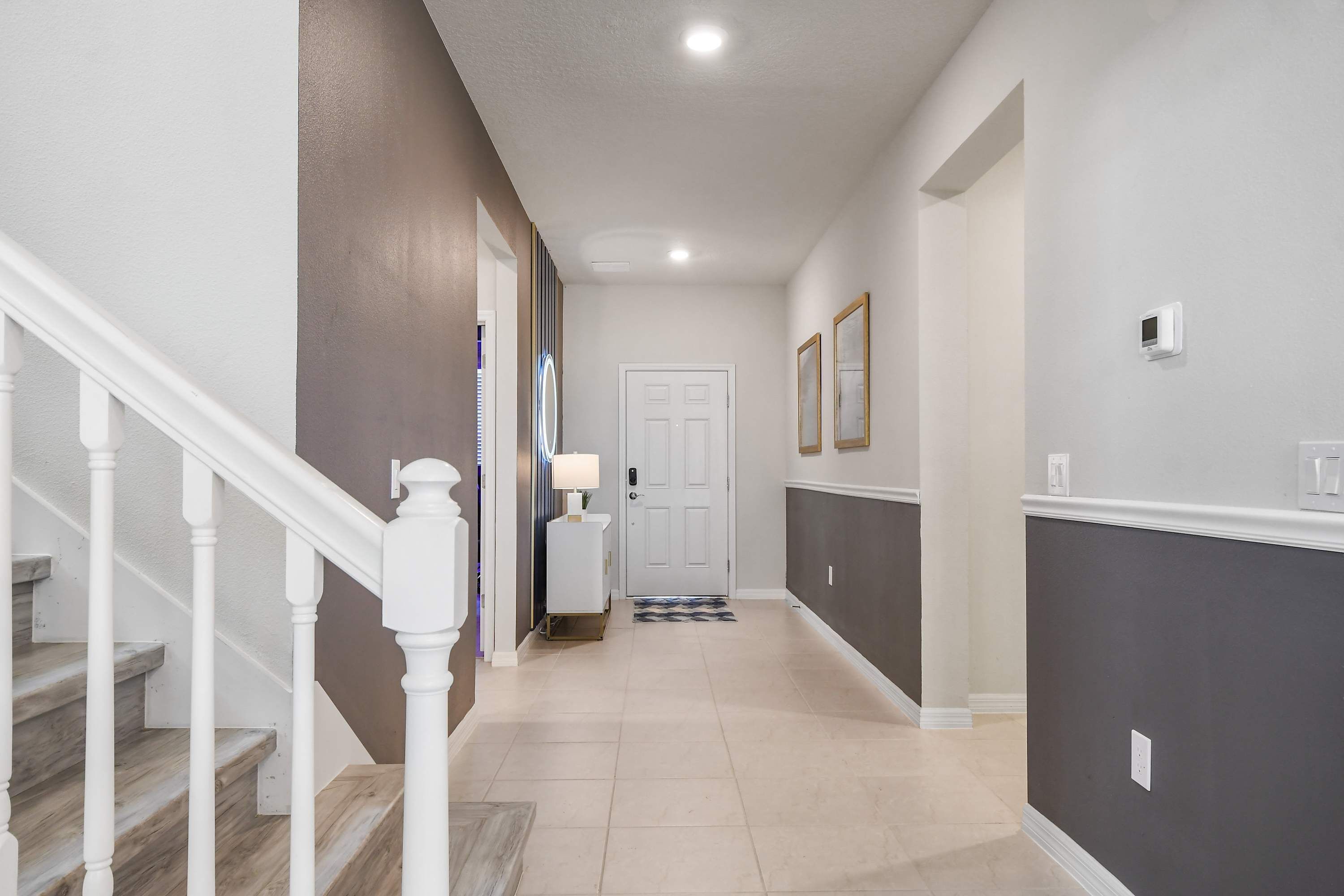 A hallway with a staircase, a door, and a wall-mounted thermostat.