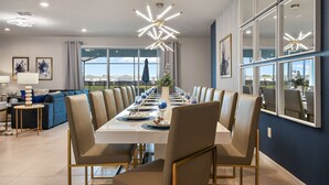 Un comedor con una larga mesa dispuesta para una comida, rodeada de sillas, y un candelabro moderno colgando sobre ella.